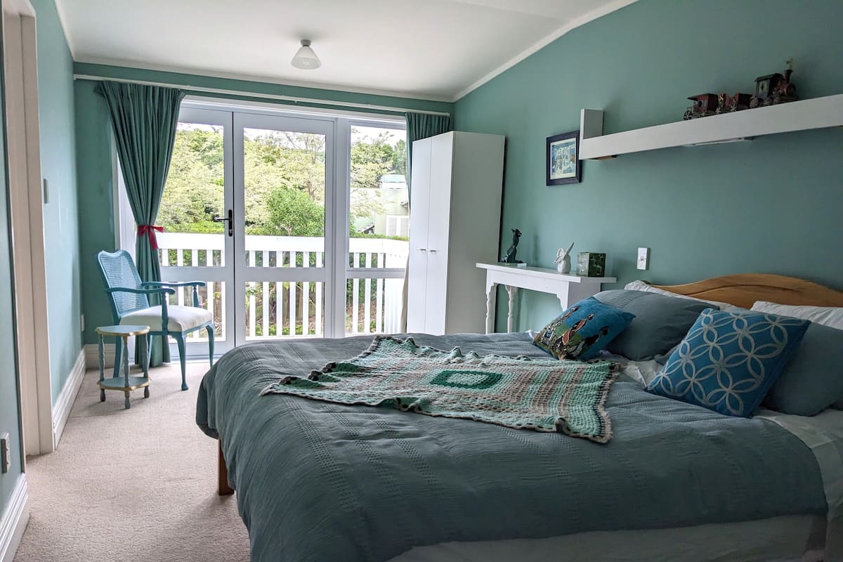 A bedroom with a large bed, a chair, a desk, and a balcony.