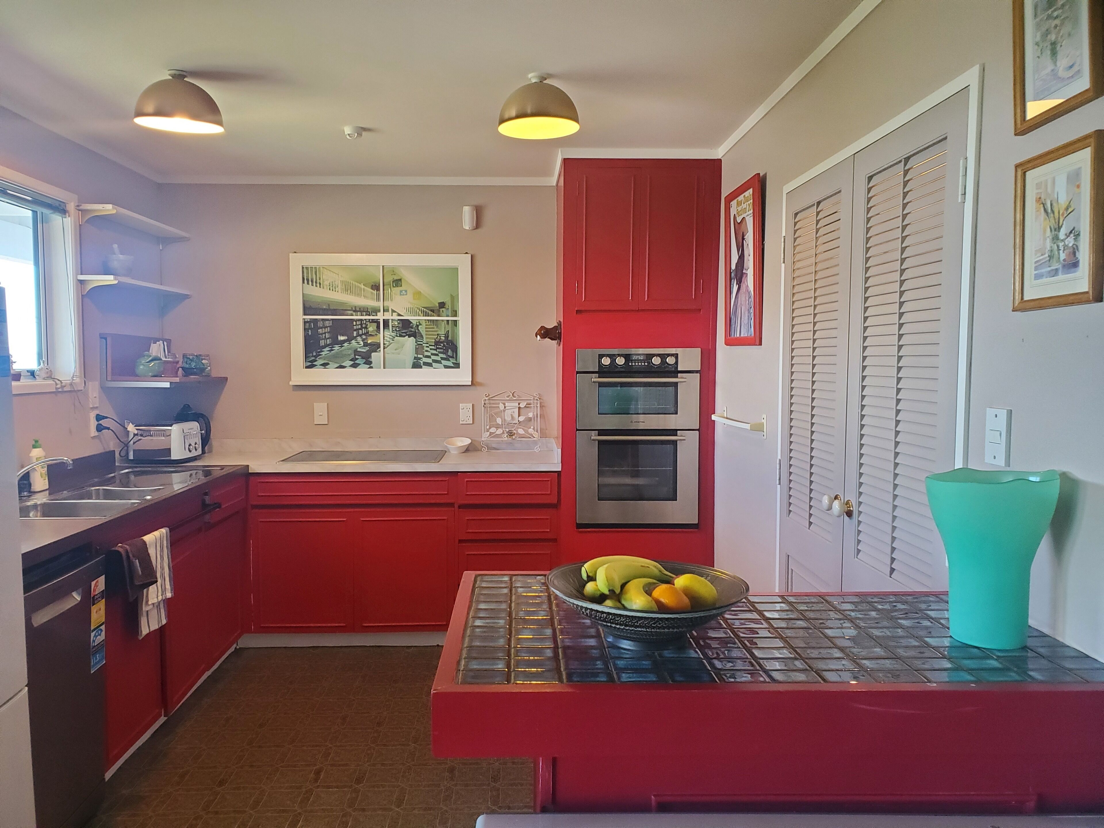 A kitchen with red cabinets, a double oven, a sink, and a fruit bowl on the counter.