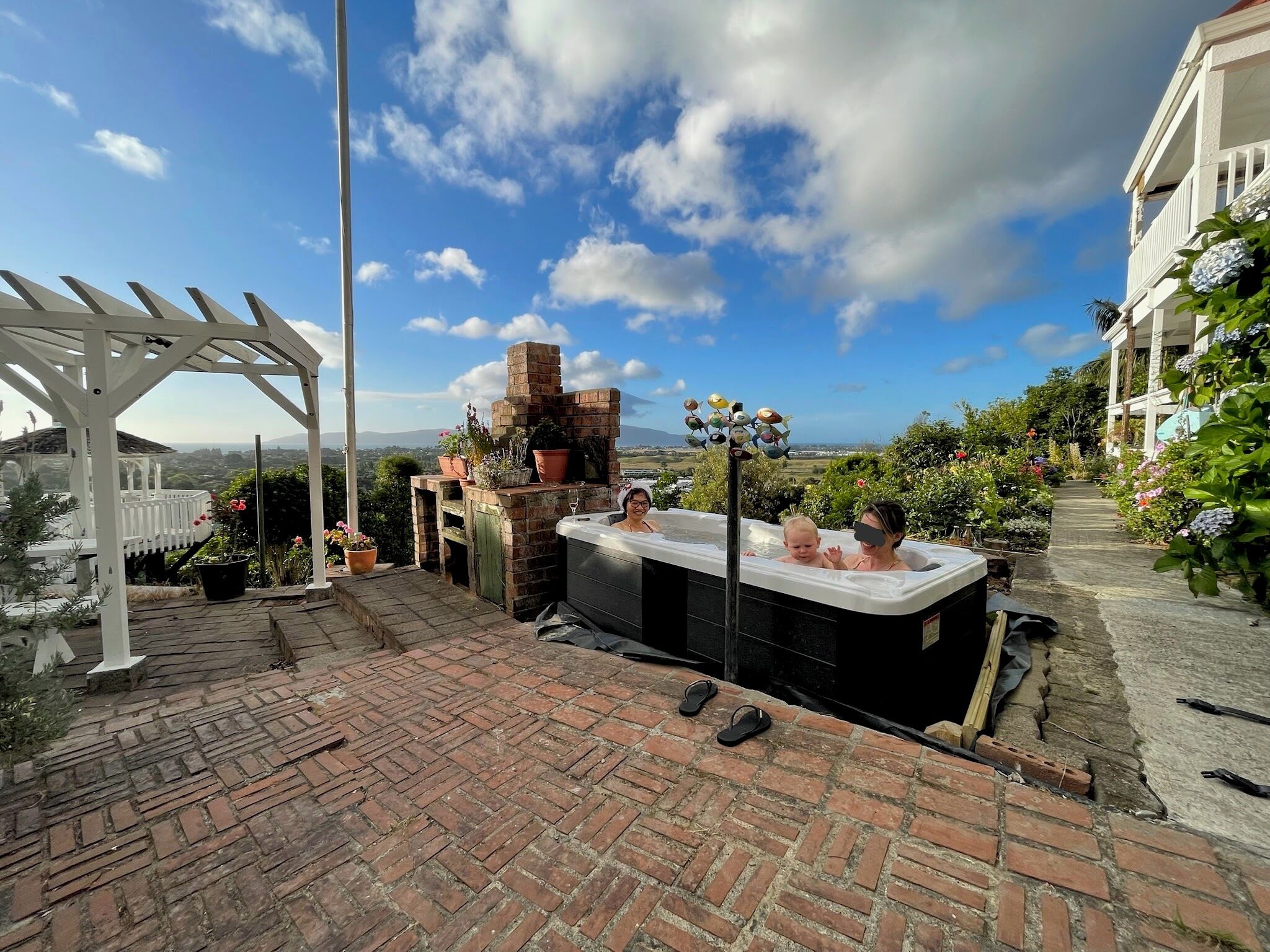 Un'area patio con idromassaggio, pavimento in mattoni, una pergola e un camino in muratura.