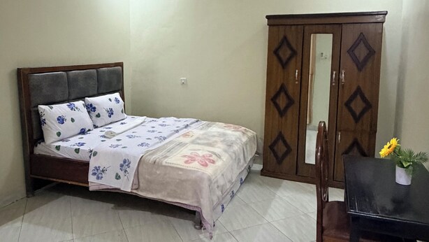A bedroom with a bed, a wardrobe, a table with a flower, and a chair.
