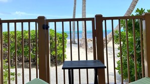 Un balcón con vistas a la playa, palmeras y una mesa.