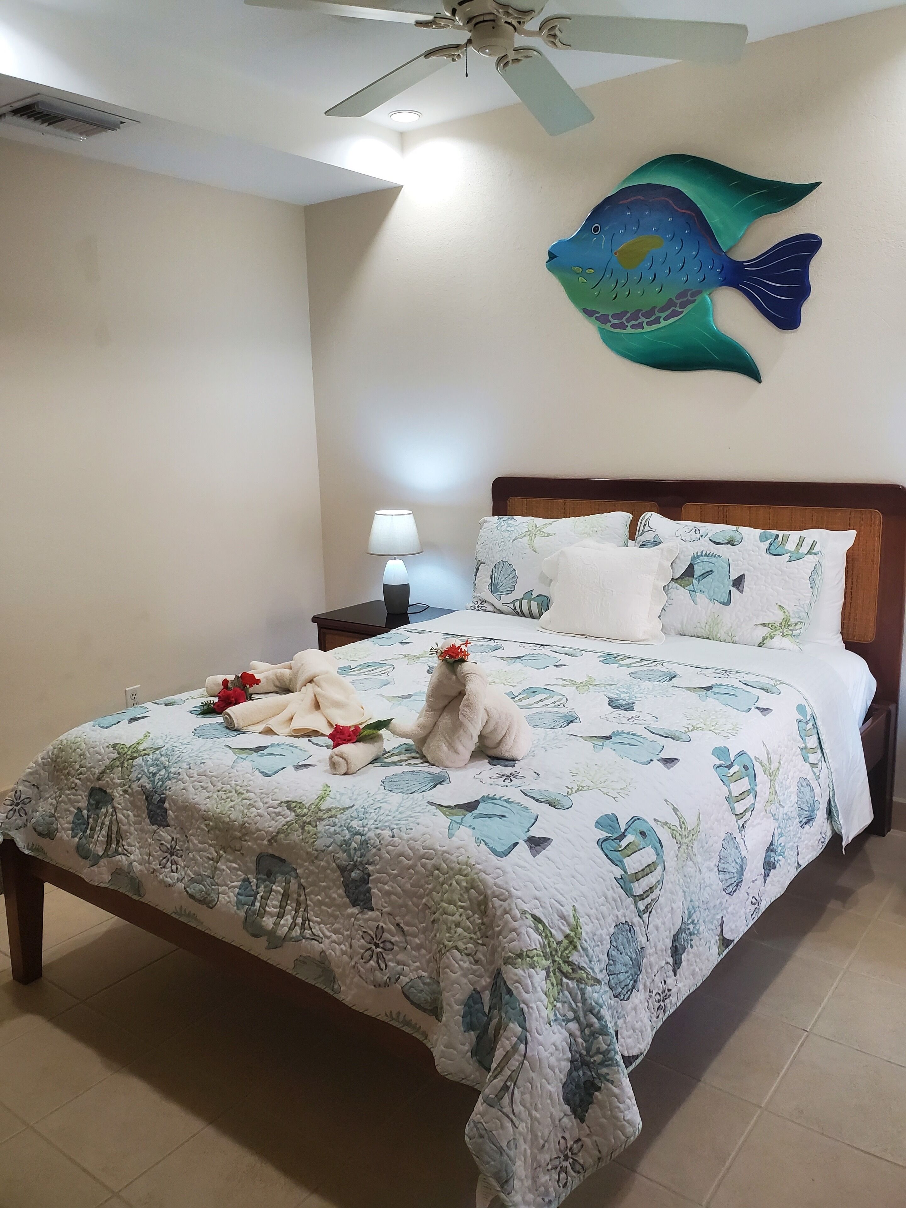 A neatly made bed with a floral quilt, a nightstand with a lamp, and a ceiling fan.