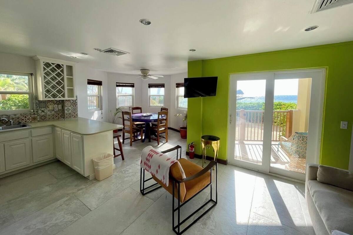 A spacious living area with a dining table, chairs, a sofa, and a TV mounted on the wall.
