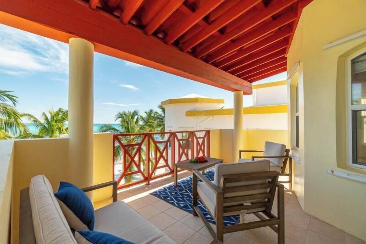 A balcony with a wooden pergola, a sofa with cushions, a small table, and a chair.