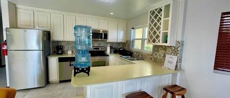 A kitchen with white cabinets, a stainless steel refrigerator, a water dispenser, and a bar stool.
