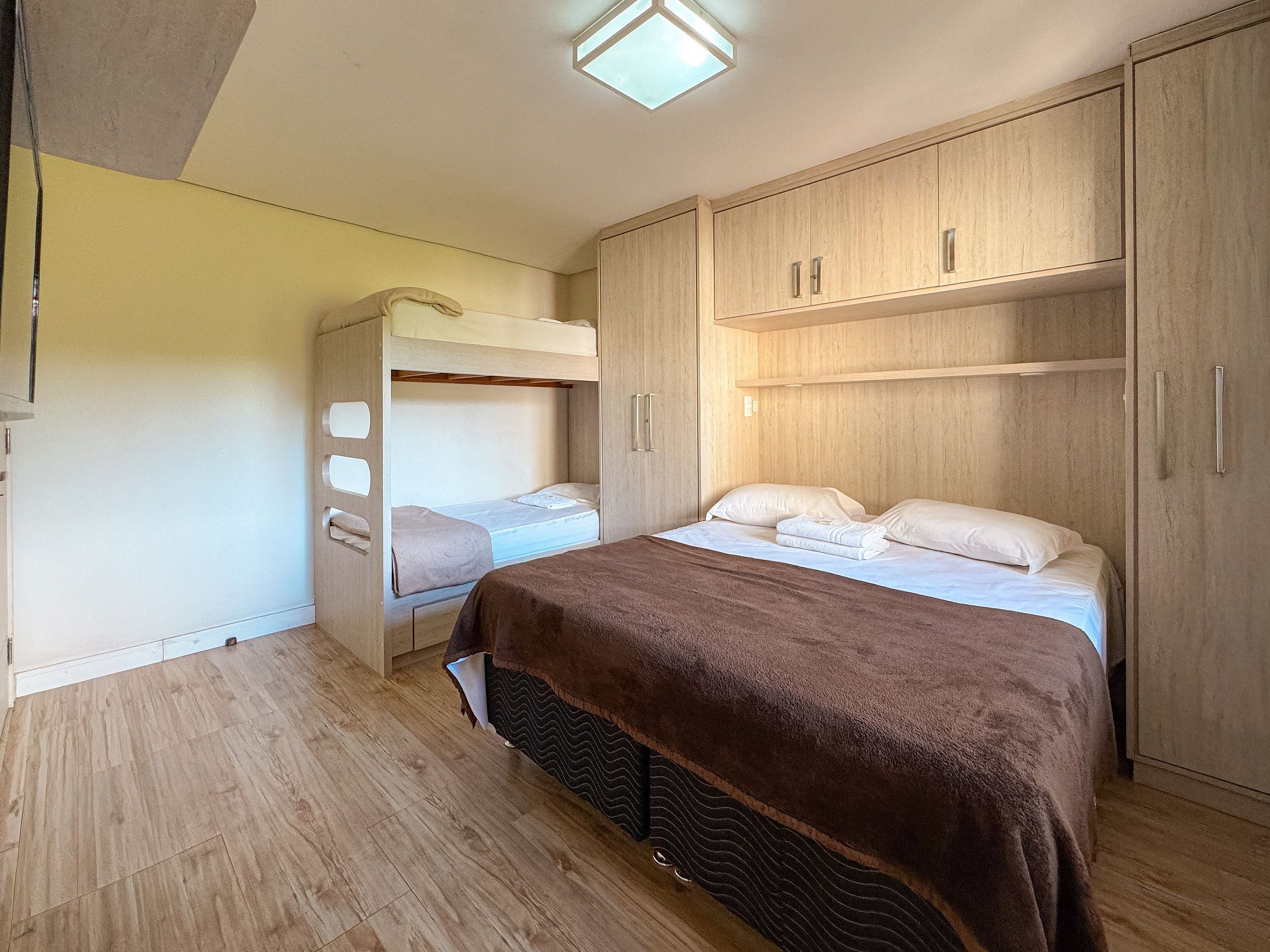 Habitación compacta con literas, cama individual y armarios empotrados de madera.