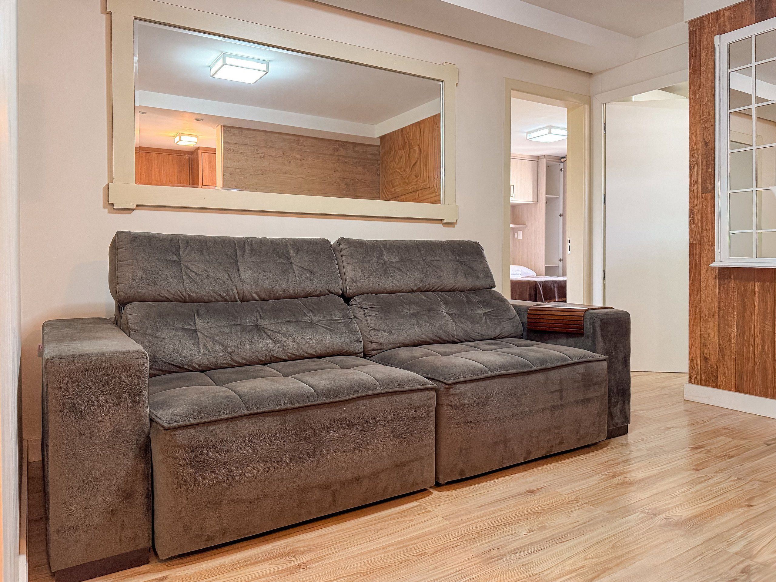 Un sofá gris en una habitación con suelo de madera y un espejo grande en la pared.