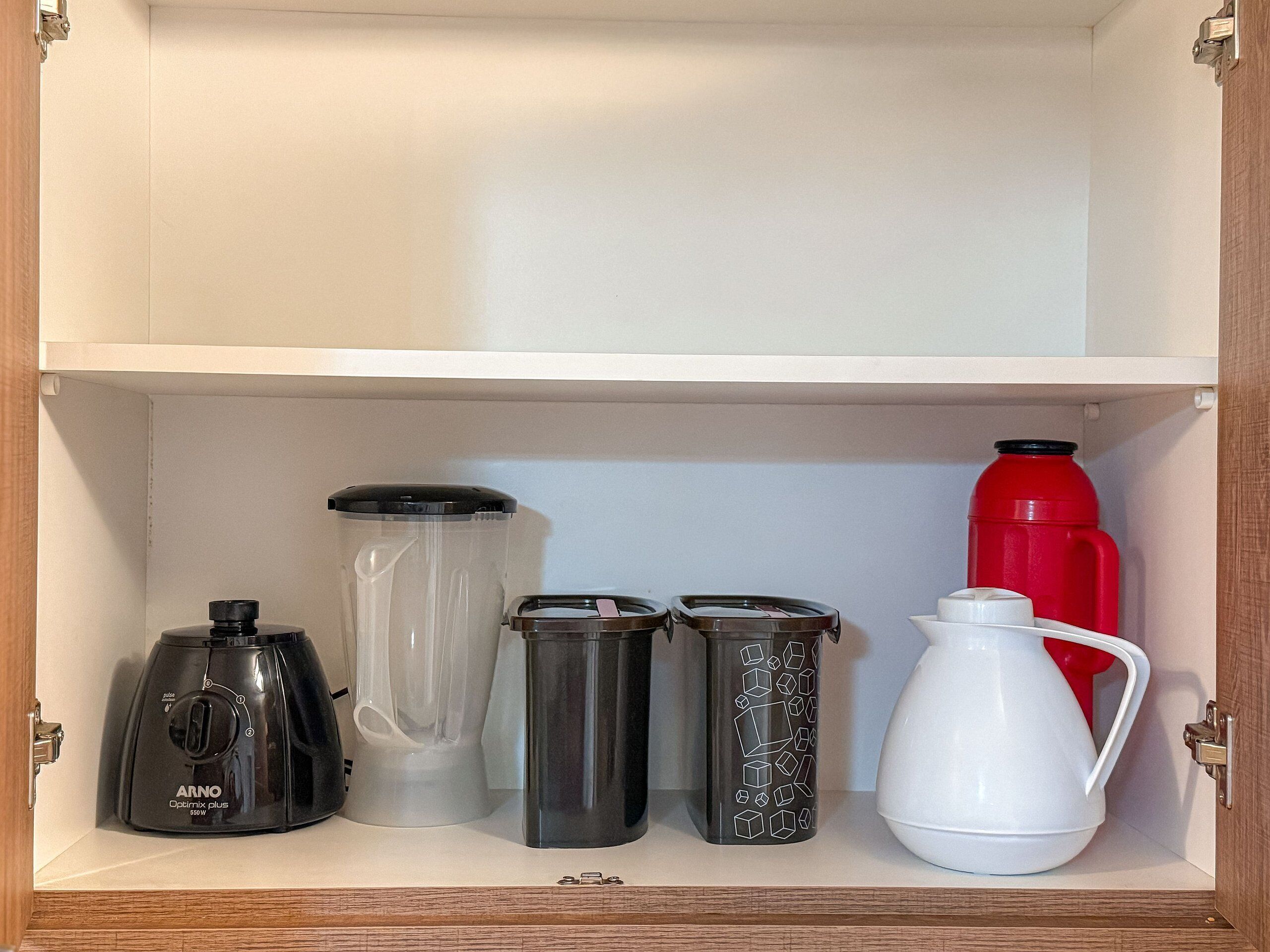 A kitchen cabinet containing a coffee maker, a blender, a kettle, and a thermos.