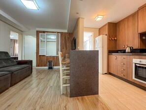 A modern kitchen with wooden cabinets, a built-in oven, and a dining area with a chair and table.