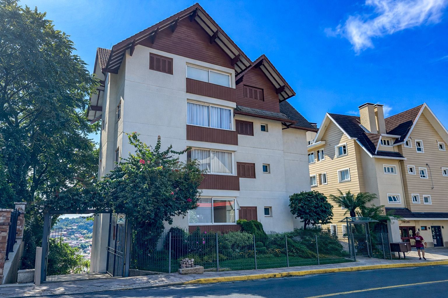 Un immeuble résidentiel à plusieurs étages, doté d’une façade blanche et de touches de couleur marron, avec des balcons et une entrée sécurisée par un portail.