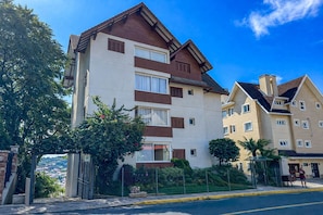 A multi-story residential building with a white facade and brown accents, featuring balconies and a gated entrance. - Risidencial Dona Rita (Gramado)