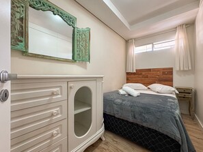 A bedroom with a bed, a dresser, a mirror, and a window with curtains.