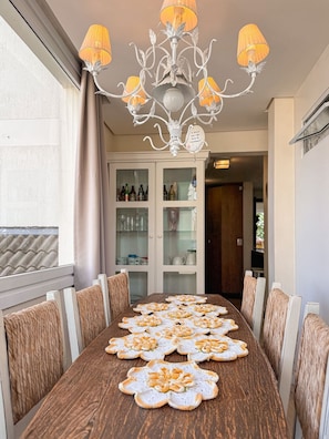 Uma sala de jantar com uma mesa de madeira, cadeiras brancas e um candelabro.