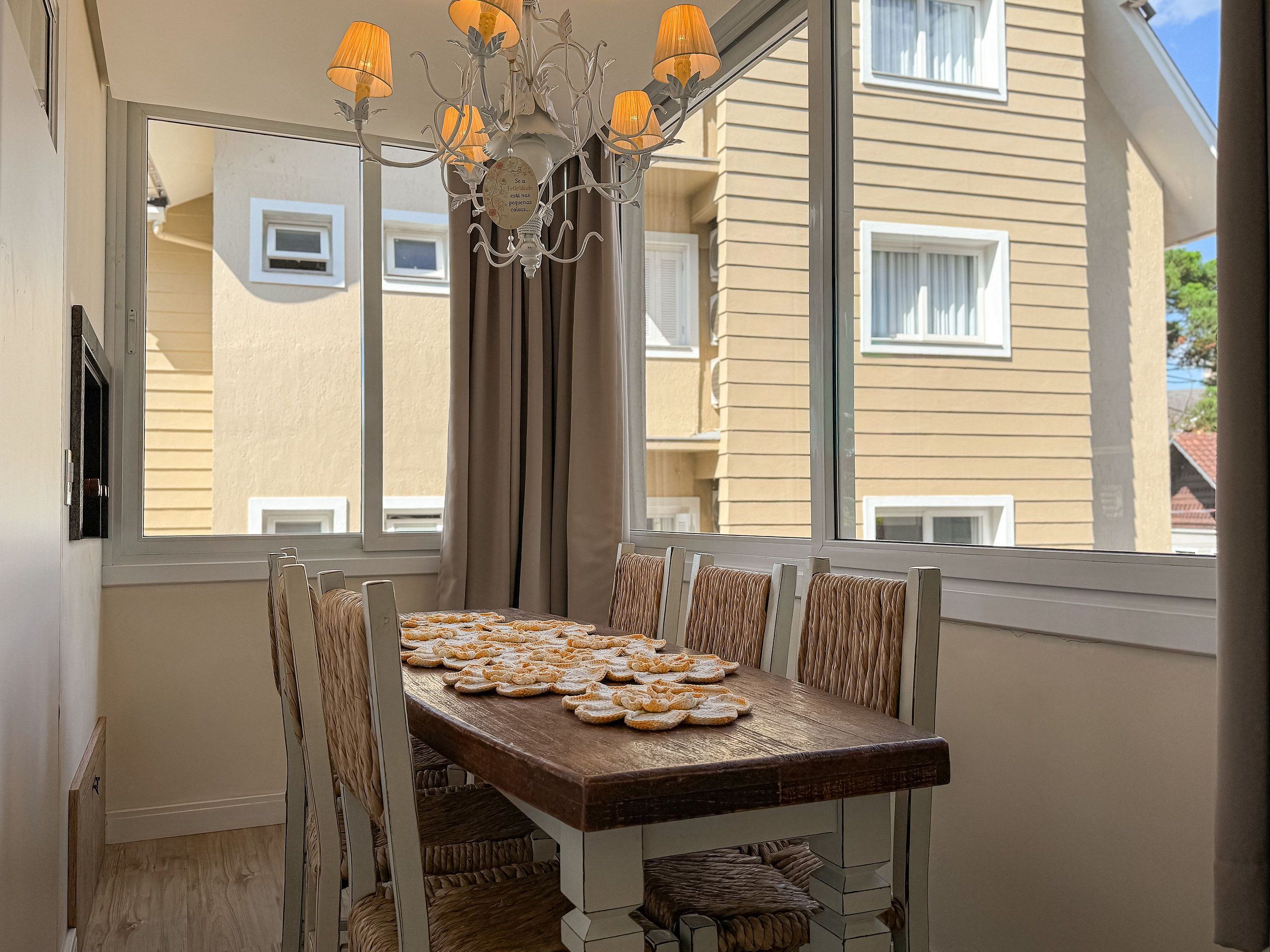 A dining table with a chandelier, curtains, and a view of neighboring buildings.