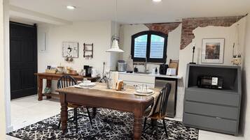 A modern kitchen with a dining area, featuring a wooden table, chairs, a black and white patterned rug, and a brick wall.