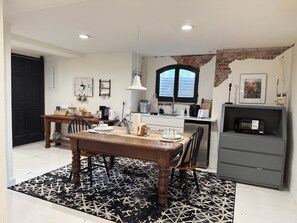 A modern kitchen with a dining area, featuring a wooden table, chairs, a black and white patterned rug, and a brick wall. - Farmhouse Suite in Willamette Valley (Salem)
