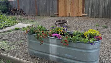 Een tuin met een metalen plantenbak vol kleurrijke bloemen, een houten omheining en een houten poort op de achtergrond.