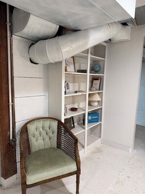 A room with a wooden chair, a white bookshelf, and a white wall with a white pipe running across it. - Farmhouse Suite in Willamette Valley (Salem)
