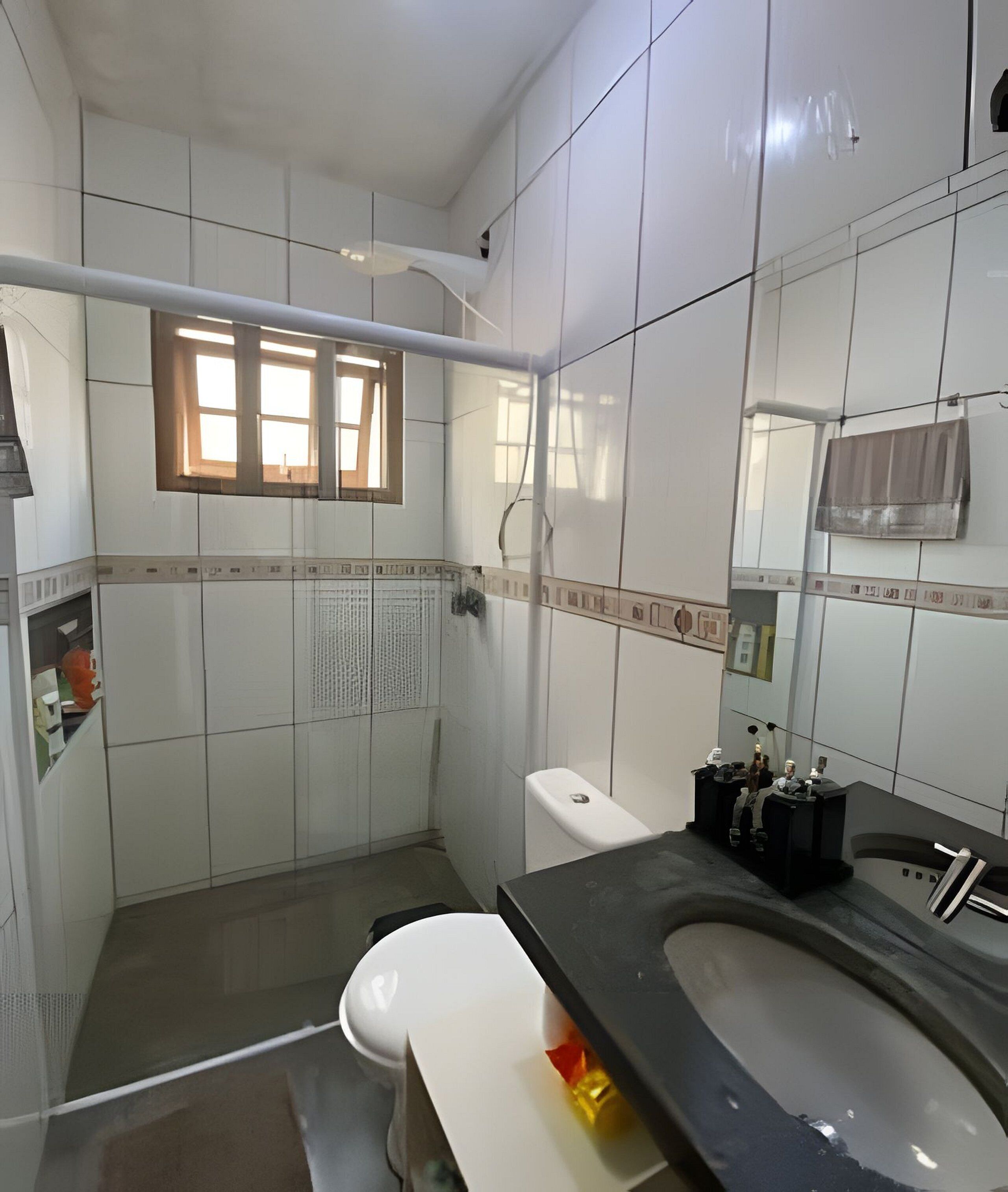A bathroom with white tiles, a toilet, a sink with a black countertop, and a window with blinds.