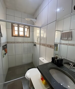 A bathroom with white tiles, a toilet, a sink with a black countertop, and a window with blinds.