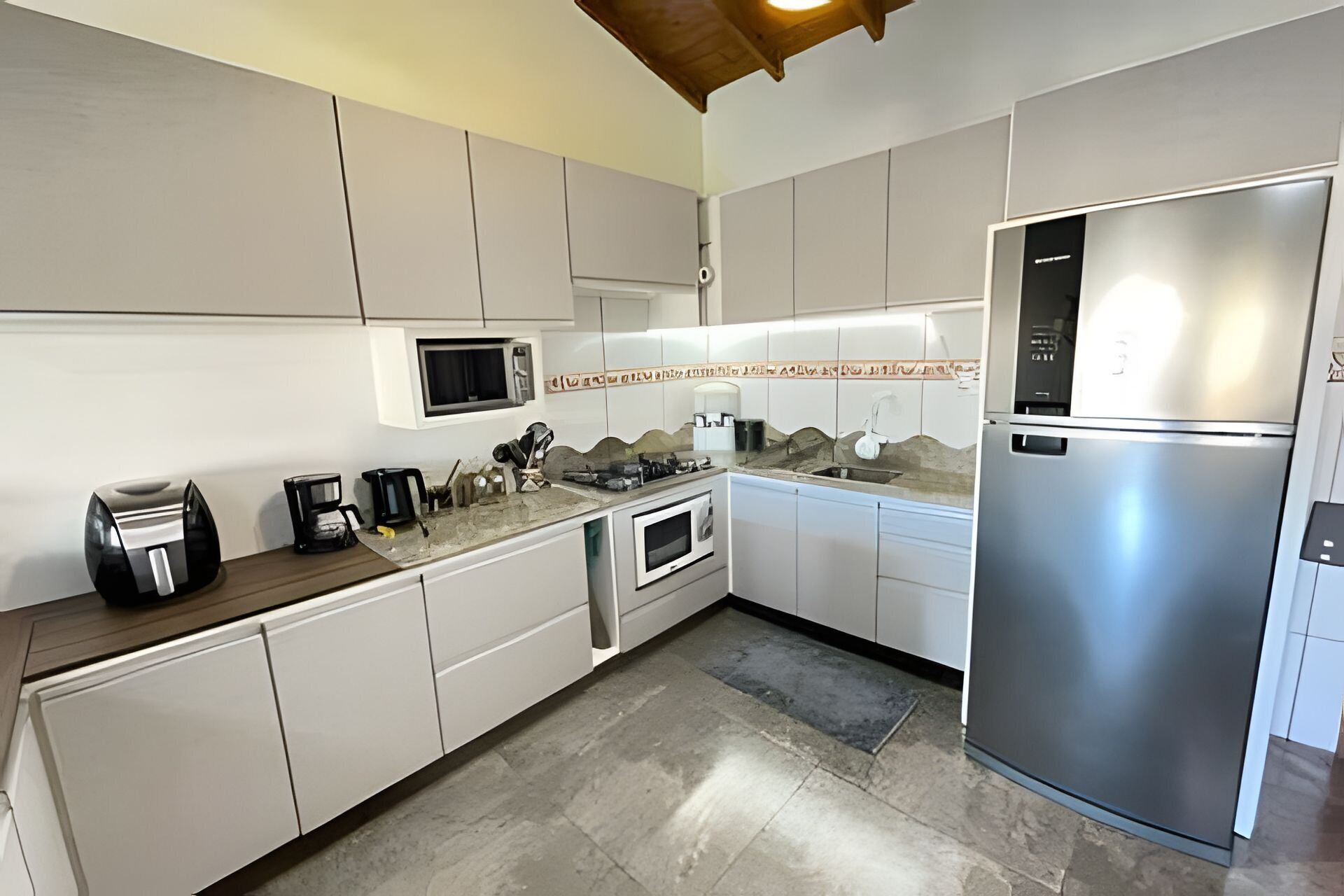 A modern kitchen with white cabinets, a stainless steel refrigerator, a microwave, a coffee maker, and a gas stove.