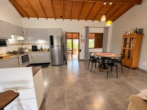 A modern kitchen with a built-in oven, a refrigerator, and a dining area with a round table and chairs. - Casa 2 Quartos - Centro - Xangri-Lá (Xangri-La)