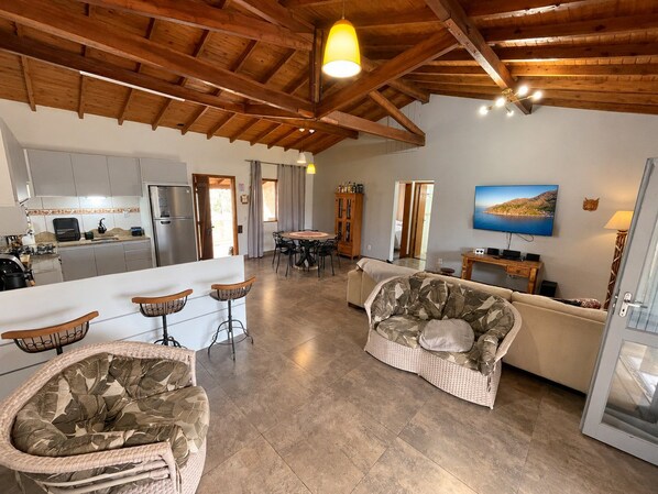 Amplia sala de estar con techo alto, cocina con electrodomésticos modernos y comedor con mesa y sillas.