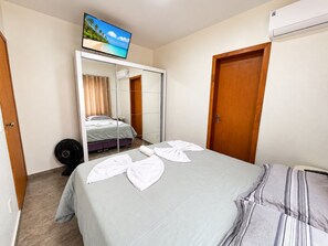 A hotel room with a bed, a television mounted on a wall, a wardrobe, and an air conditioning unit. - Casa 2 Quartos - Centro - Xangri-Lá (Xangri-La)