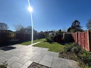 En terrasse med stenfliser, græsplæne og en murstensmur.