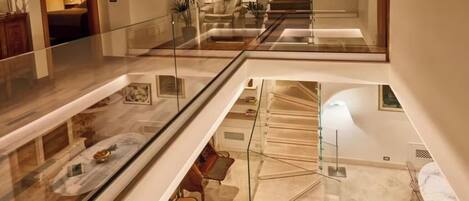 A spacious, multi-level interior with a glass railing, a dining area with a marble table, and a staircase leading to an upper level.