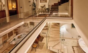 Un intérieur spacieux à plusieurs niveaux, doté d’une balustrade en verre, d’un coin repas avec une table en marbre et d’un escalier menant à un niveau supérieur.