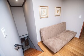 Ein Zimmer mit einem beige farbenen Sofa, Holzboden und zwei gerahmten Kunstwerken an der Wand.