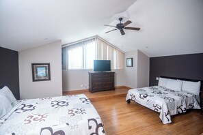 Ein Schlafzimmer mit zwei Betten, einem Deckenventilator, einem Fernseher auf einer Kommode und einem Fenster mit Vorhängen.