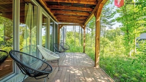 A covered porch with wooden beams, large windows, and two chairs.