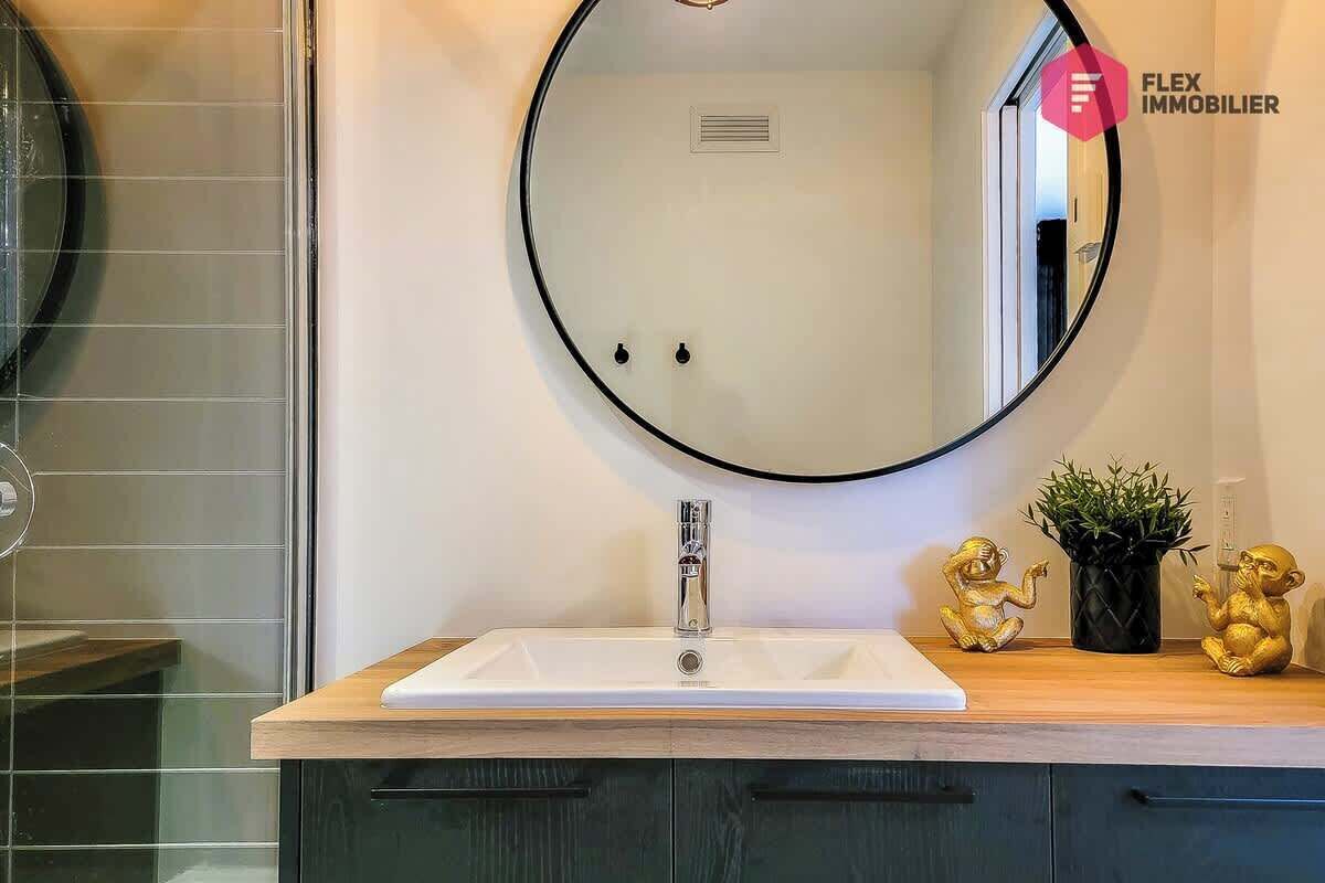 A bathroom with a round mirror, a white sink, and a wooden countertop. There are two golden statues on the countertop.
