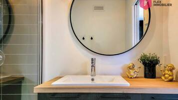A bathroom with a round mirror, a white sink, and a wooden countertop. There are two golden statues on the countertop.