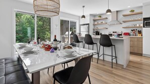 Een moderne keuken met een eethoek, grote ramen en uitzicht op groen.