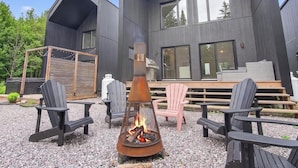 Een moderne buitenruimte met Adirondack-stoelen, een vuurkorf en een terras met uitzicht op een modern gebouw.