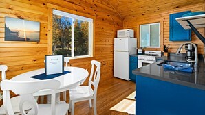 Une cuisine chaleureuse, aménagée dans le style d’un chalet, avec des murs en bois, un coin repas doté de chaises blanches, un réfrigérateur, une cuisinière et un évier.