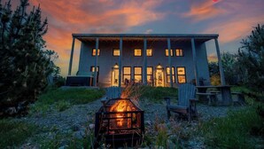 A modern house with a fire pit in the front yard, surrounded by trees.