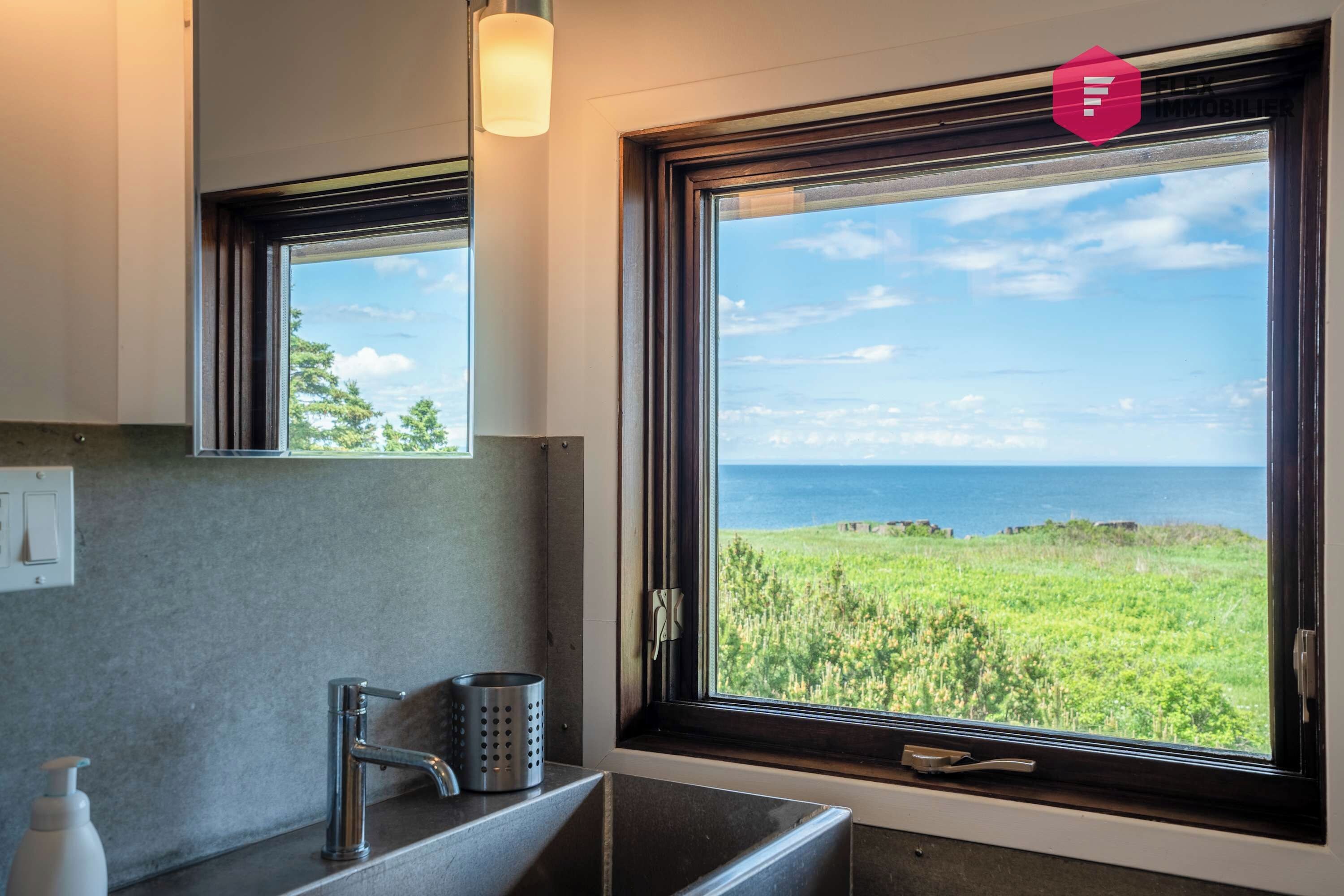 Une salle de bain avec une grande fenêtre, un lavabo, un miroir et un robinet.
