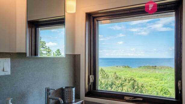 A bathroom with a large window offering a view of the sea and greenery.