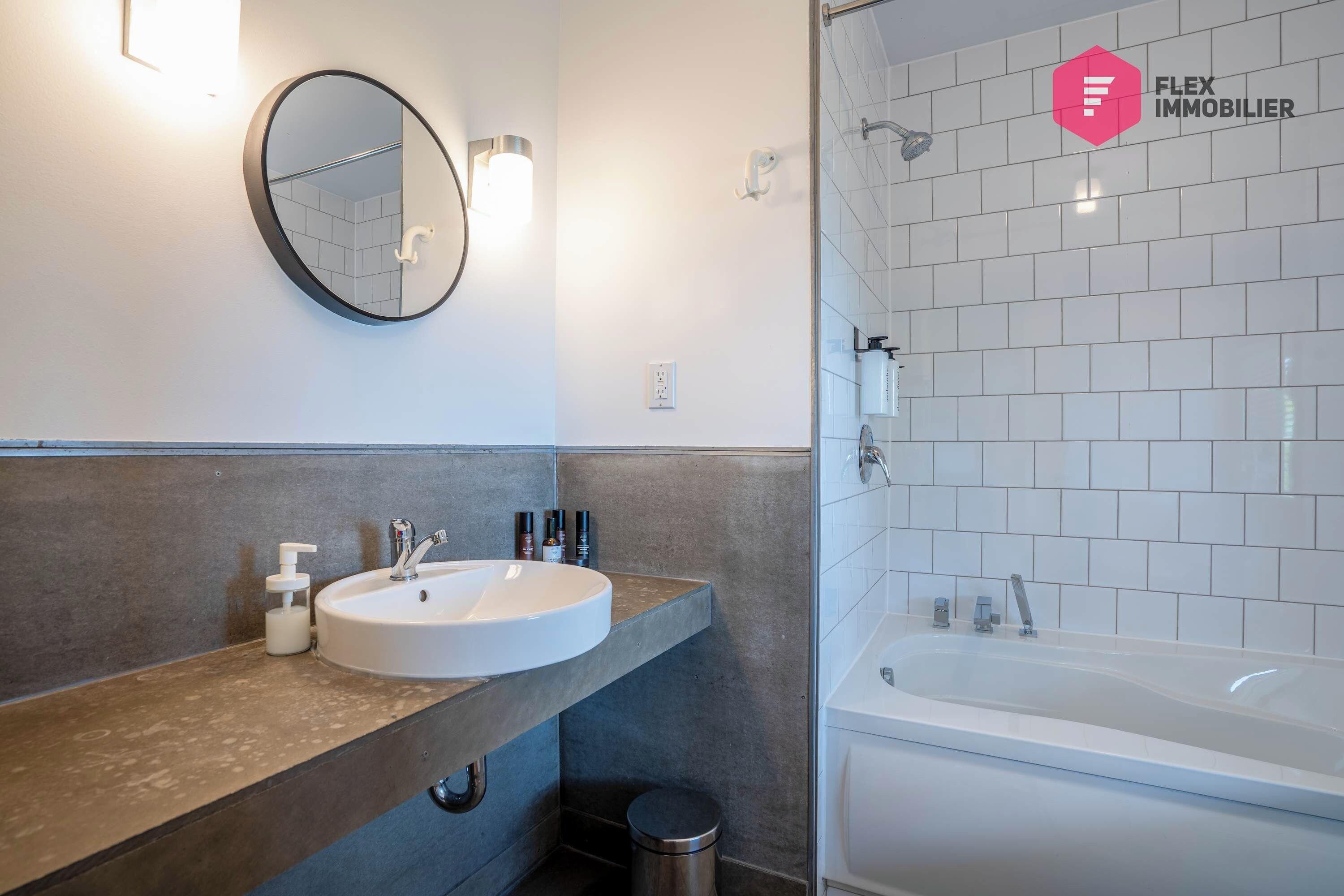 A modern bathroom with a round mirror, a sink with a soap dispenser, and a bathtub.