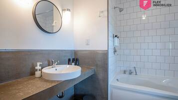 A modern bathroom with a round mirror, a sink with a soap dispenser, and a bathtub.