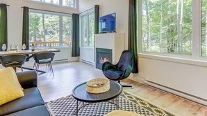 A modern living room with a fireplace, large windows, and a dining area. - The Sunny-Haus in Portneuf - Private hot tub, Pool (Pont-Rouge)