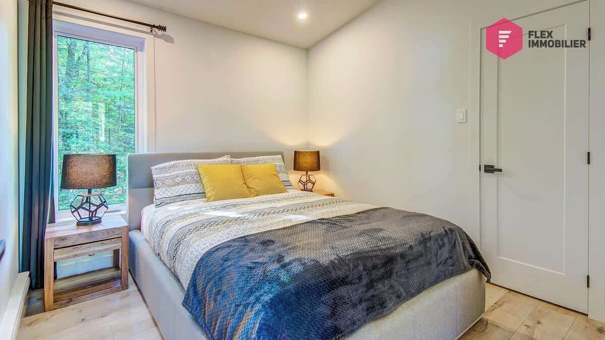 Une chambre à coucher avec un lit, des lampes de chevet, une fenêtre avec des rideaux et une porte ornée d’un logo.