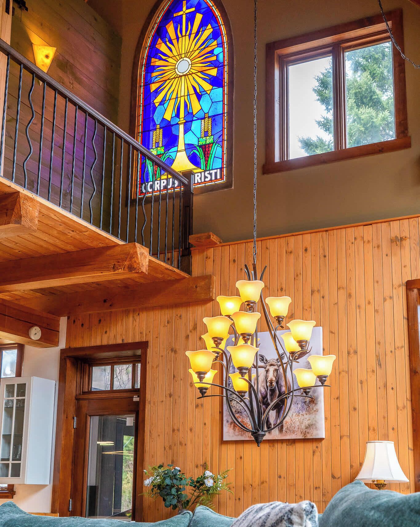 A wooden interior with a stained glass window, a chandelier, and a painting of a moose.