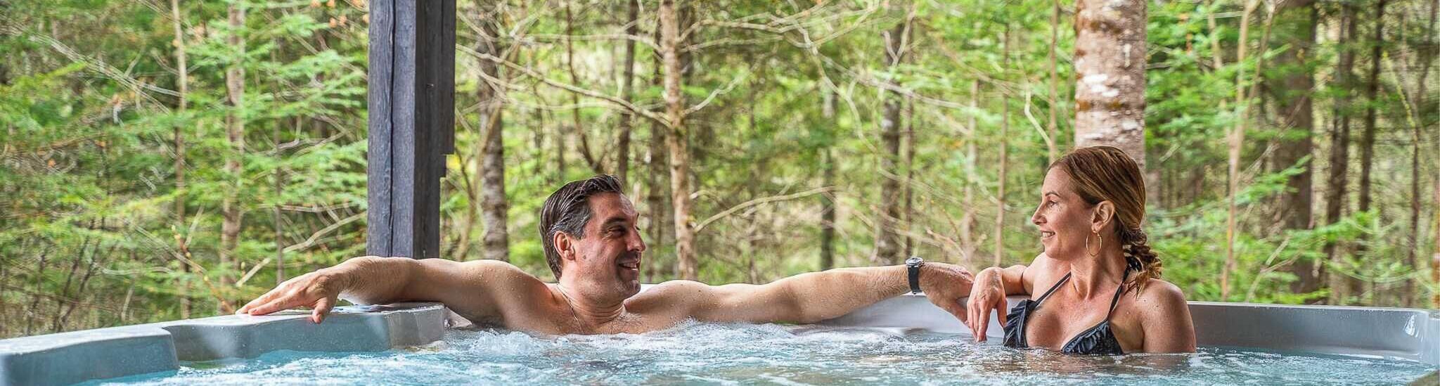 A couple in a hot tub surrounded by a forest.