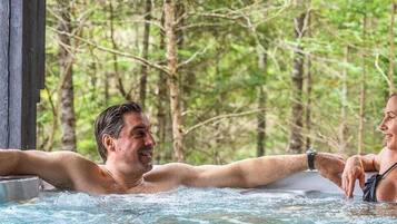 A couple in a hot tub surrounded by a forest.