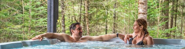 Un couple dans un jacuzzi, entouré d’une forêt.